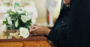 Woman in black veil placing white rose on top of casket