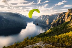 paraglider gliding over the mountains and a river with a green parachute