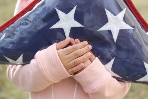 young girl in a pink sweater holding a trifold American flag