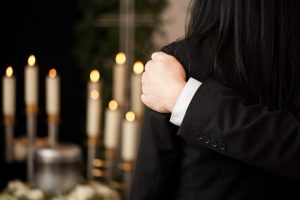 Close up of someone's arm on someone else's shoulder from the back, lit candle sticks in the background