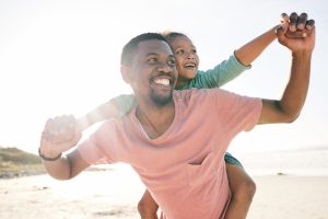 AA image- father and daughter playing piggyback on a beach and laughing