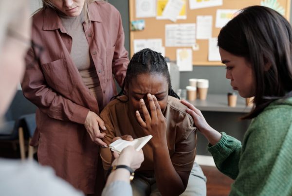 A woman crying with her hand in front of her face while people surround and support her.