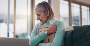 A woman sadly clutching a picture frame to her chest.