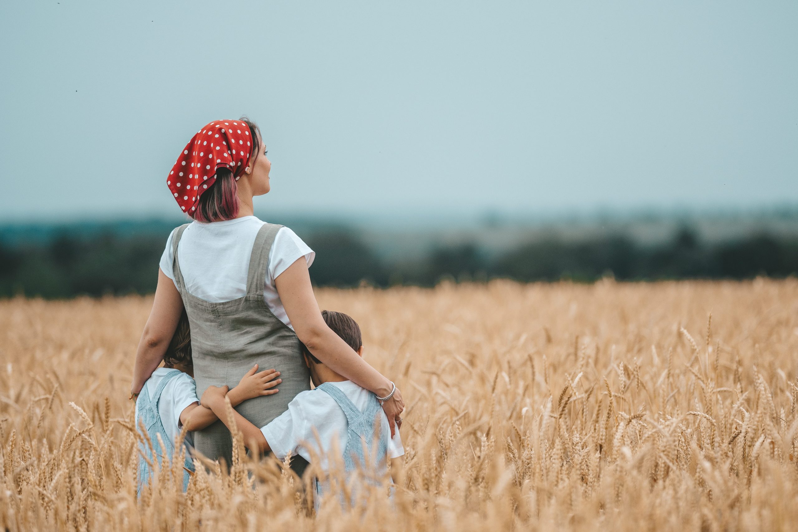 mom and two kids standing in a field and gazing out to the trees