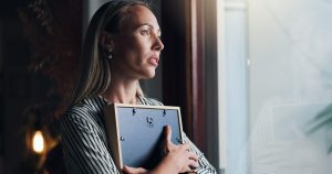 woman holding a framed photograph while looking out a window