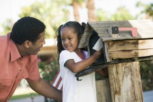 A little girl and her father placing a letter in a mailbox.
