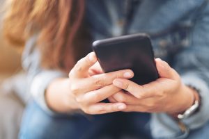 woman with long brown hair texting on a black phone