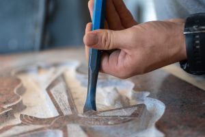 Man using a hand tool to carve a design on a headstone