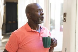 Man holding a coffee mug and looking out the window.