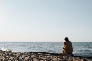 man sitting alone on a beach looking out onto the water