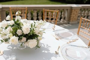 White flower arrangement on a table with a white tablecloth, and gold chairs around it