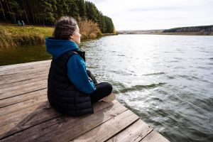 Woman sitting crossed legged on a dock and looking out over a lake.
