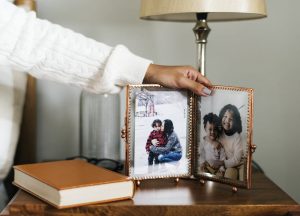 Picture frame, book, and lamp on a table, someone's hand resting on the frame.