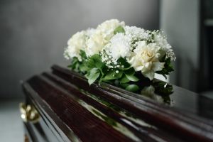 Dark wood casket with flower spray of white flowers resting on top