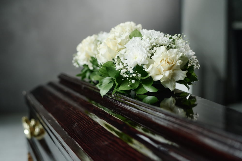 Dark wood casket with flower spray of white flowers resting on top