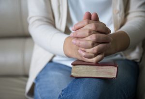 A close up of a woman sitting with her hands clasped on top of a book