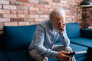 Close up of elderly man sitting on a couch and looking at a photo in his hand.