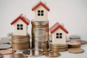 Tiny toy houses with red roofs resting on top of stacks of coins