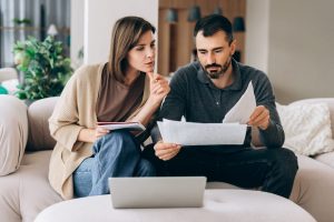 Husband and wife sitting on couch at home reviewing estate planning documents