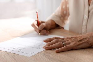 Woman in cream cardigan signing her last will and testament