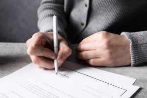 Woman in gray sweater, signing a last will and testament