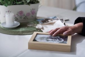 Hand on a picture frame with a photo of an elderly person resting on a table.
