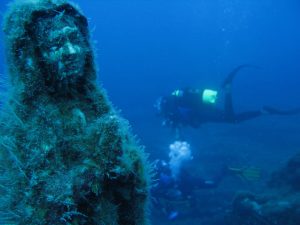 Underwater praying statue with diver in the background
