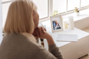 Woman gazing at a picture frame with a photo and candle on a table.